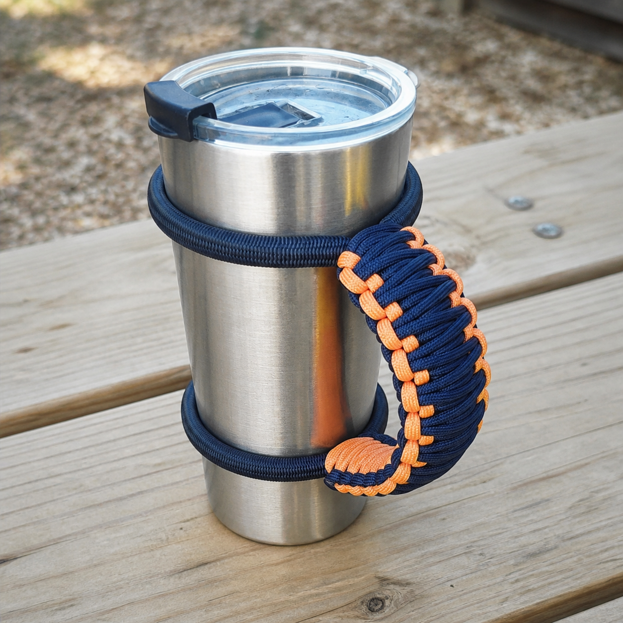 A finished stainless steel mug standing upright with a paracord handle attached.